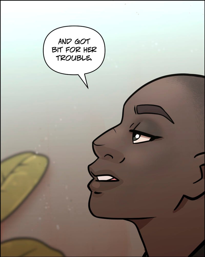Close-up of Detective Aâ€™isha, a bald Black woman, speaking with a serious expression. Sheâ€™s partially turned to the side, her gaze steady. The softly lit hospital background includes a blurred leafy plant behind her.